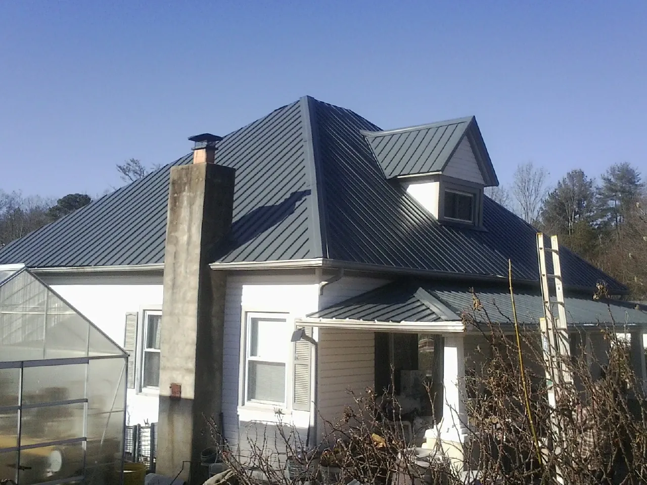 Dark blue standing seam metal roof on a white farmhouse with dormer — Slate & Tile Roof Repair by Roofing Brothers in Clanton