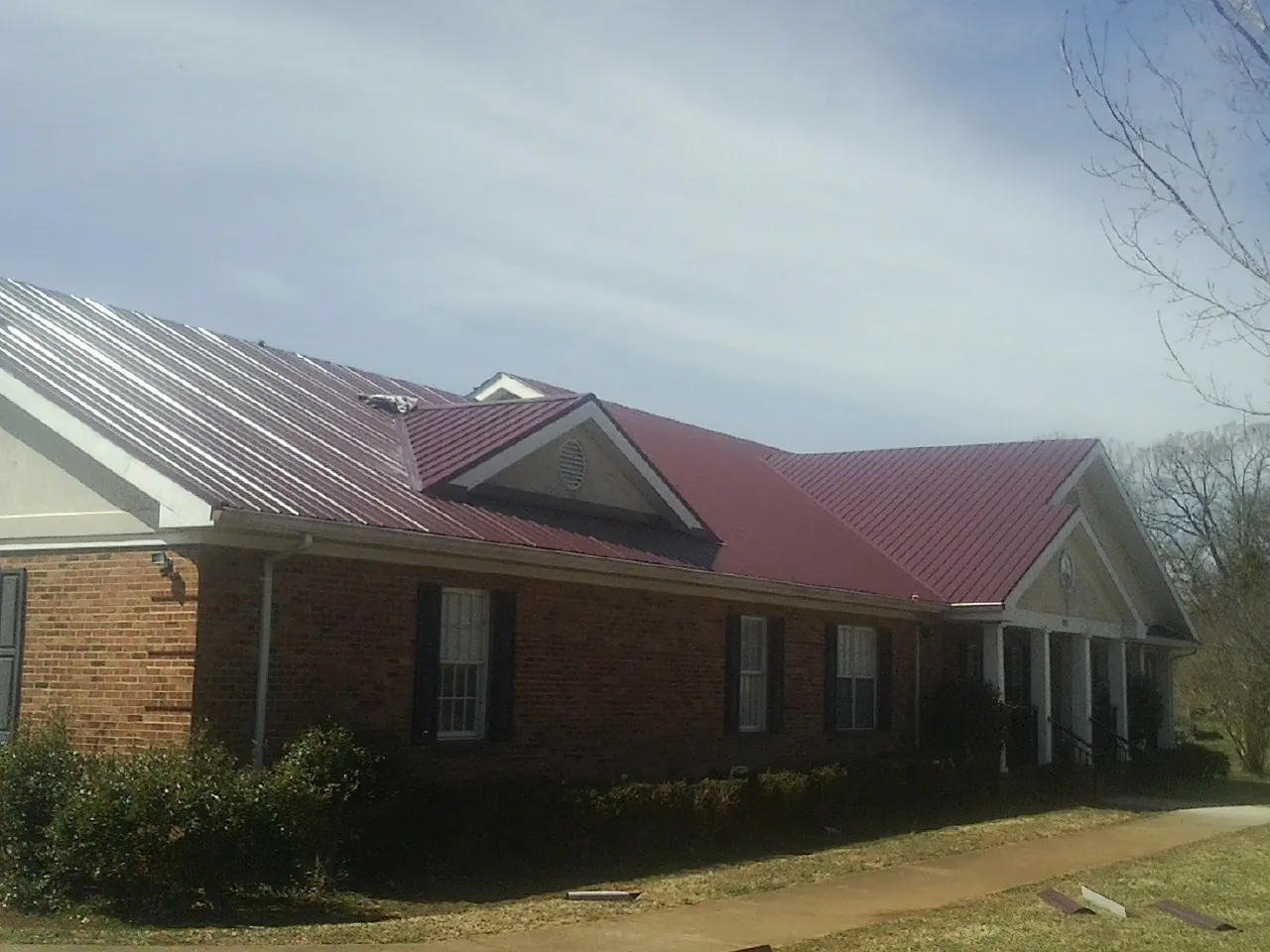 Red metal roof with gabled entries on a long brick building, from a Hail Damage Roof Repair job in Clanton