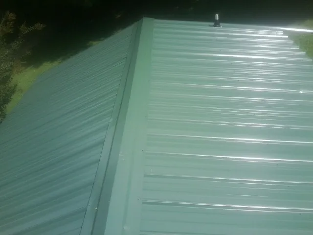 New green metal panels meeting at the ridge of a roof — Flat Roof Repair work by our crew in Clanton
