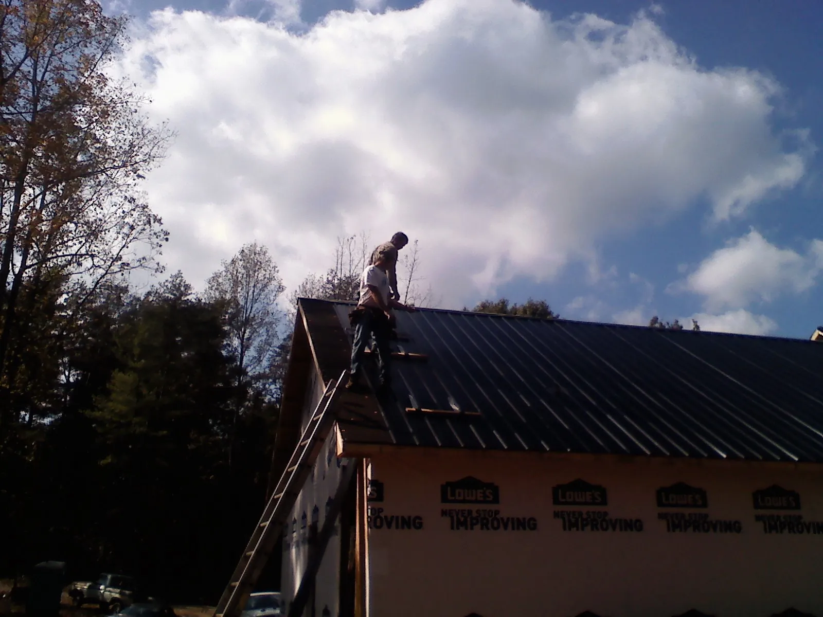 Roofer fastening dark metal panels high against a cloudy sky, from a Roof Inspection job in Clanton