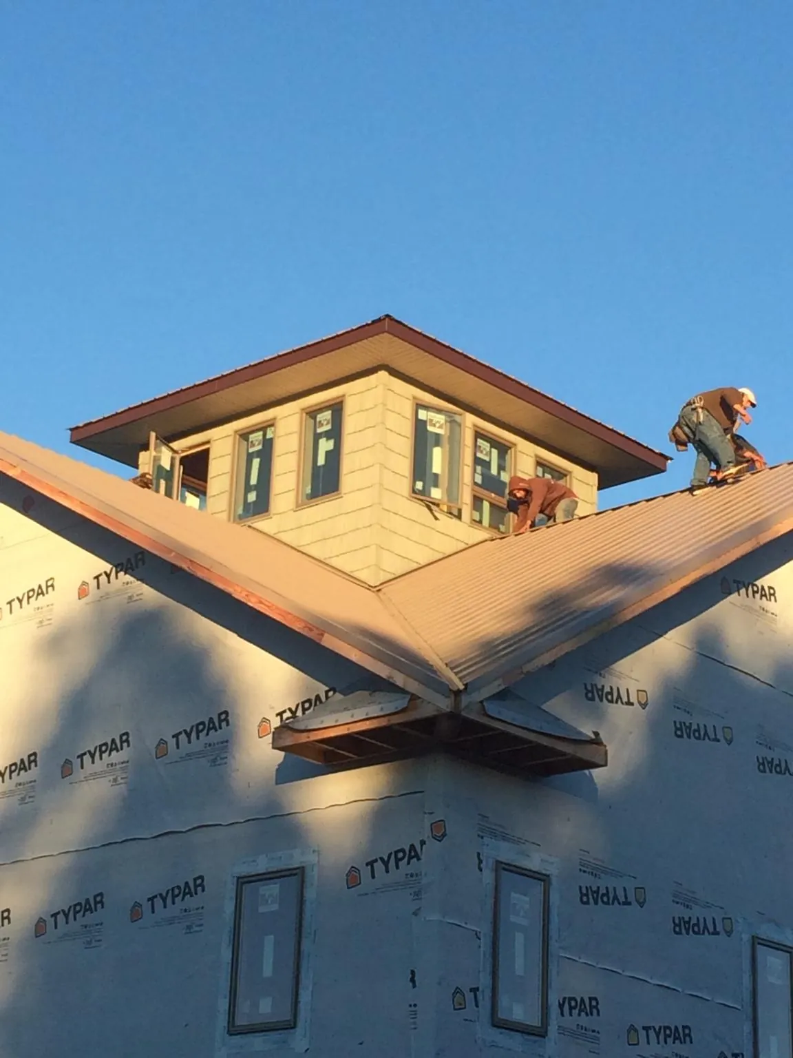 Roofers working around a rooftop cupola on a new metal roof at sunset — Roof Waterproofing in Clanton by Roofing Brothers